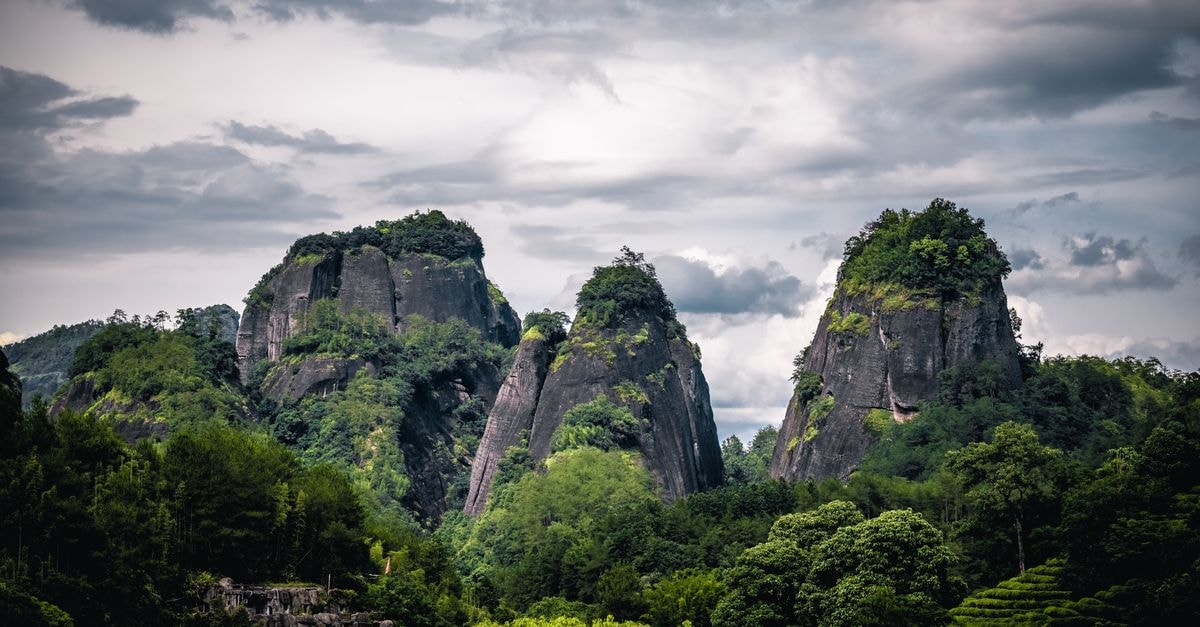 Hezhou Travel Guide: Forest Peaks and Hakka Flavors Capture of dramatic mountain peaks with lush greenery and cloudy sky.
