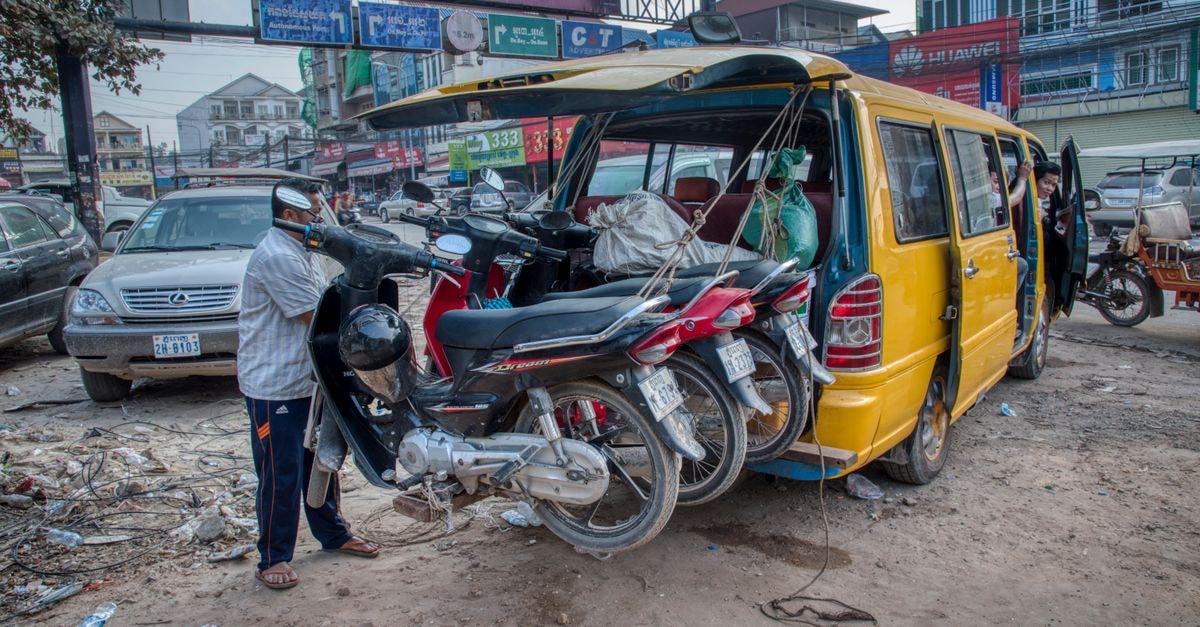 Suong Travel Guide: A Calm Look at Cambodia’s Market Town Motorcycles being loaded onto a van in a busy urban street scene, capturing the essence of daily transport.