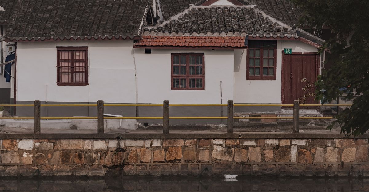 Jingzhou Travel Guide: Walls, River Light, and Quiet Hubei Charm Charming traditional house with tiled roof by a calm river, reflecting rustic architecture.