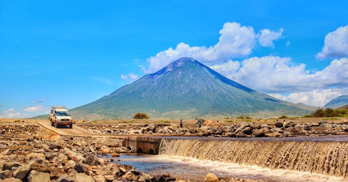 Ol Kalou travel guide: a quiet Kenyan highland town worth slowing down for A rugged vehicle crosses a rocky riverbed with the majestic Mount Meru in the background, showcasing Tanzania's wild landscapes.