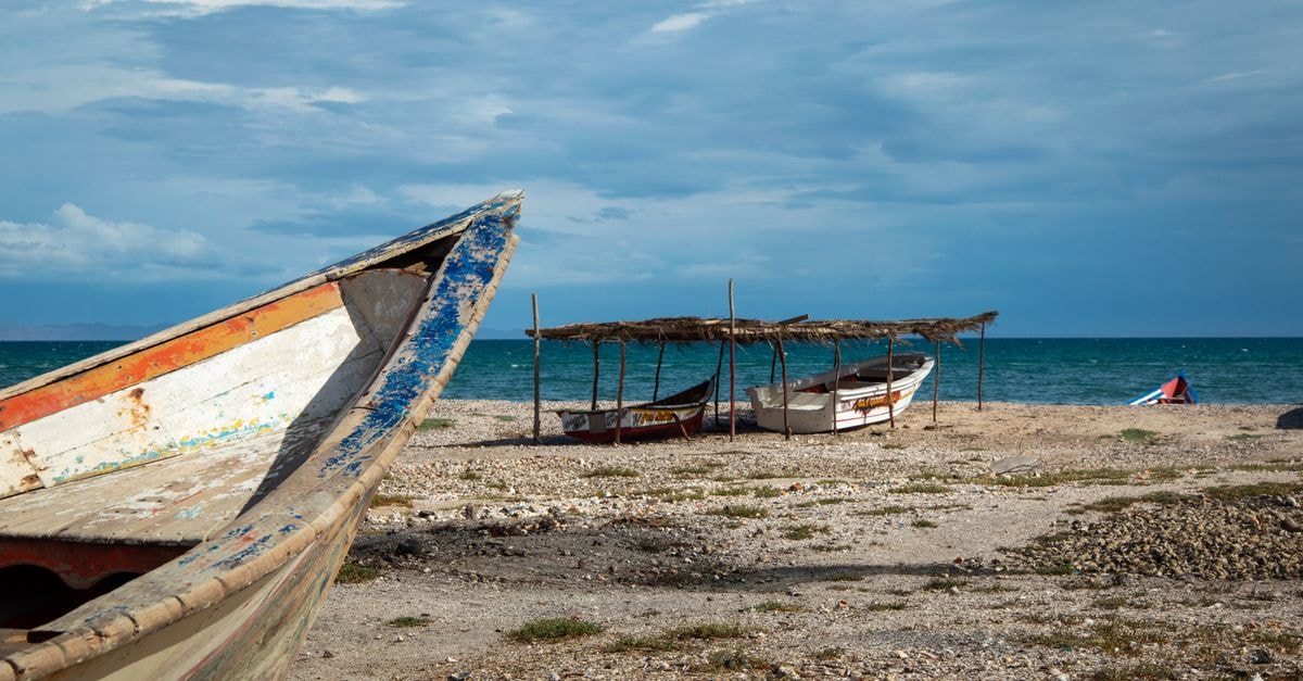 Massawa, Eritrea: A Slow Travel Guide to the Pearl of the Coast Weathered fishing boats resting on a rocky beach by the sea under a cloudy sky.