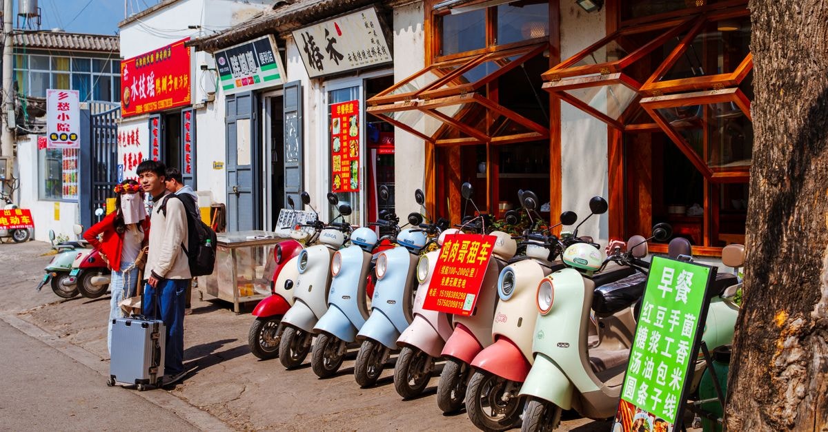 Travelers exploring a lively street with scooters in a picturesque area.