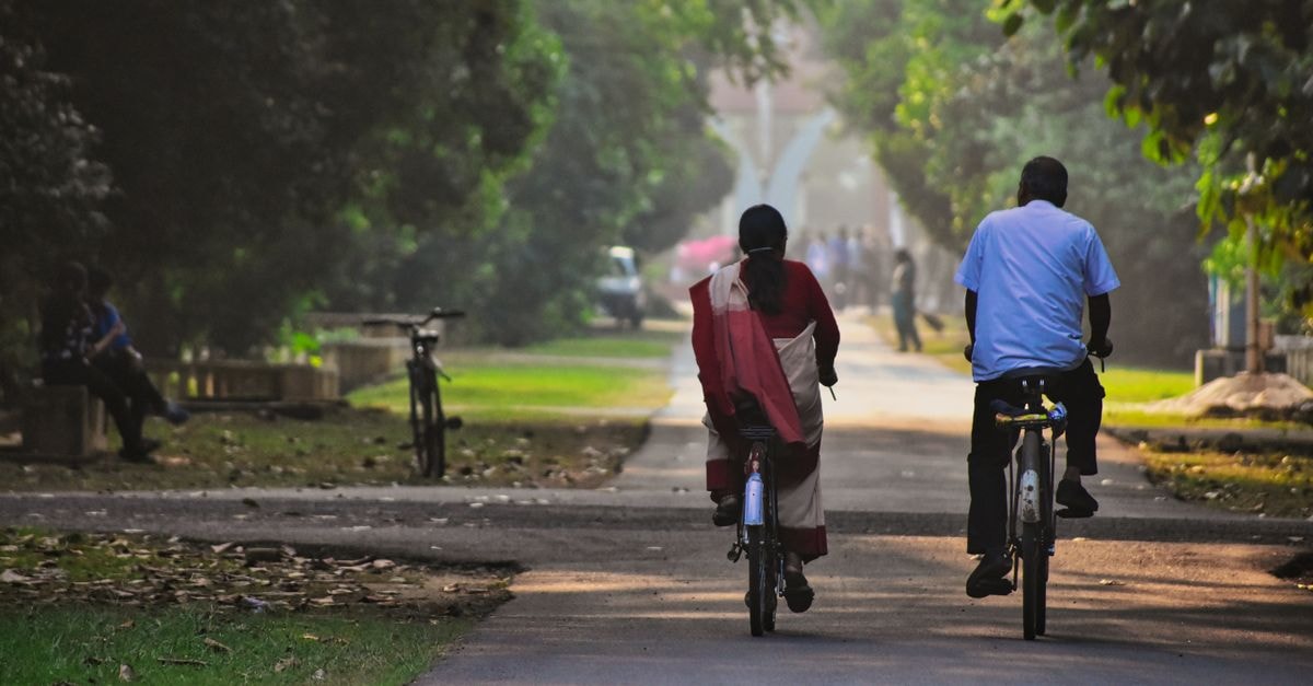 A couple rides bicycles down a tranquil park path in Rourkela, India, surrounded by lush greenery.