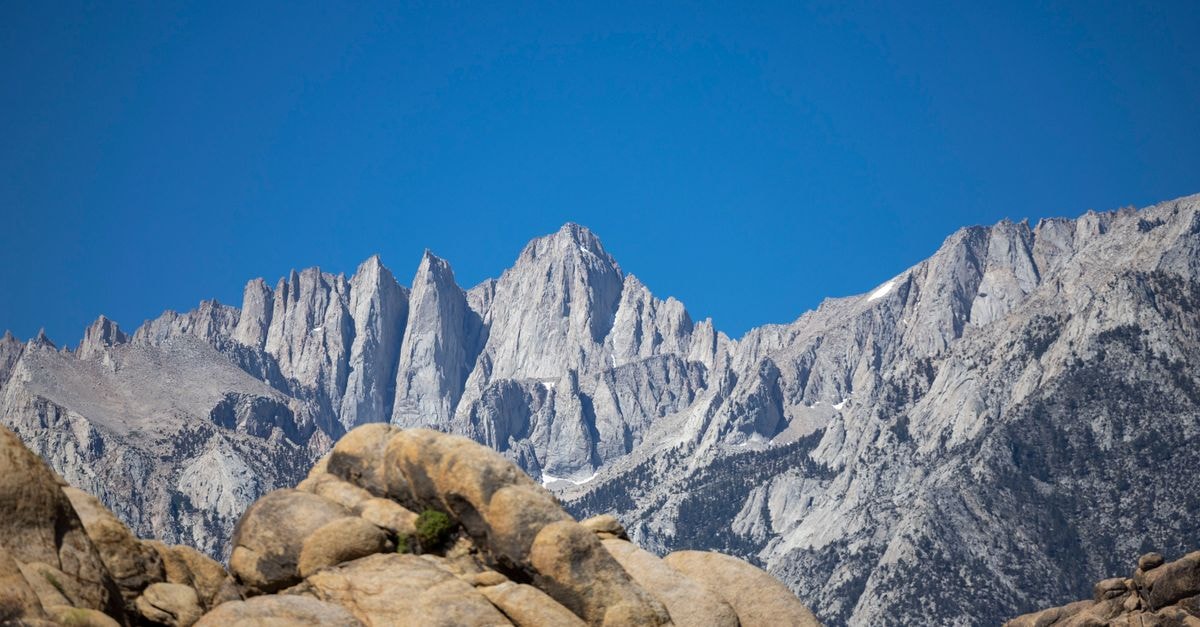 Capture the majestic Mount Whitney with its rugged peaks against a clear blue sky, showcasing natural beauty.