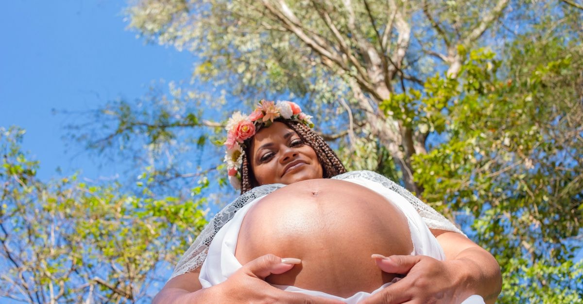 Linx Galeão Hotel, Duque de Caxias — A Poolside Pause Near Rio A joyful pregnant woman wearing a flower wreath, smiling in an outdoor setting with trees and blue sky.