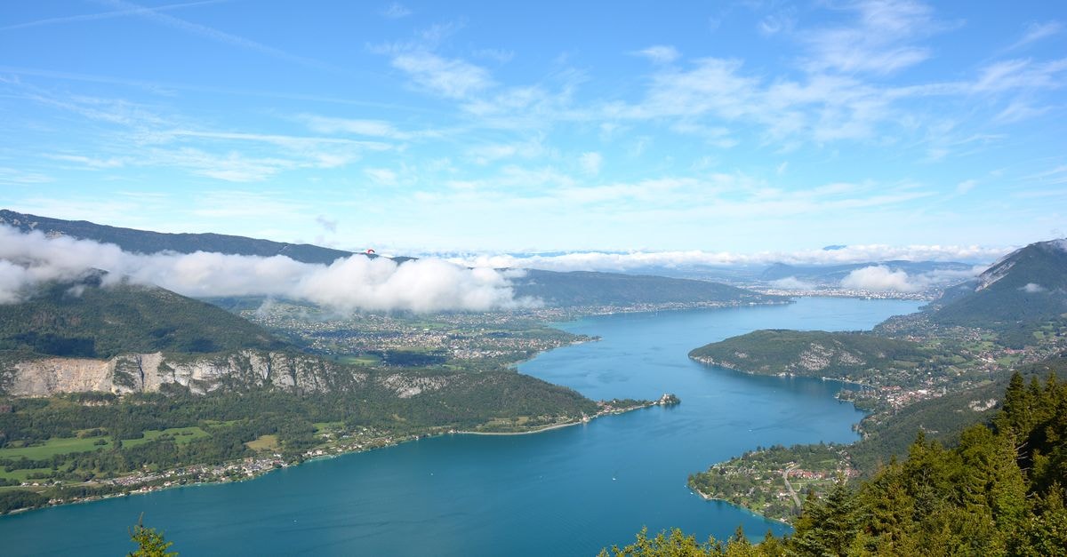 Annecy Travel Guide: Alpine Calm by France's Clearest Lake A breathtaking aerial view of Lake Annecy surrounded by lush forests and mountains under a clear blue sky.