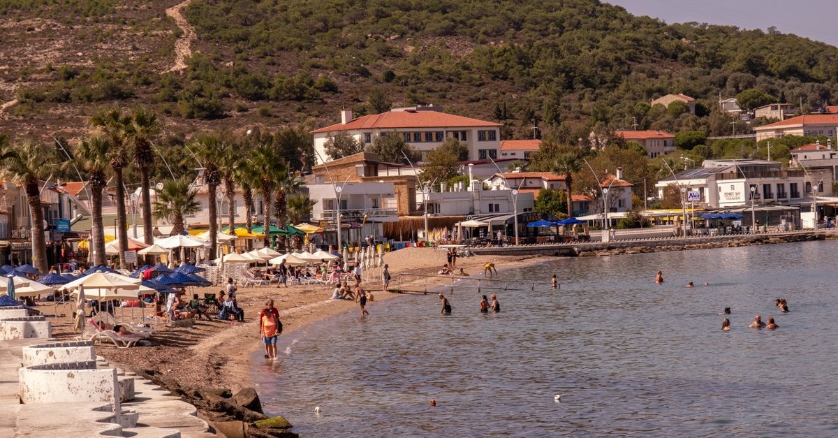 Skikda Travel Guide: Planning Tips, Costs and Things to Do People enjoying a sunny day at the beach in Foça, İzmir, surrounded by scenic hills and palm trees.