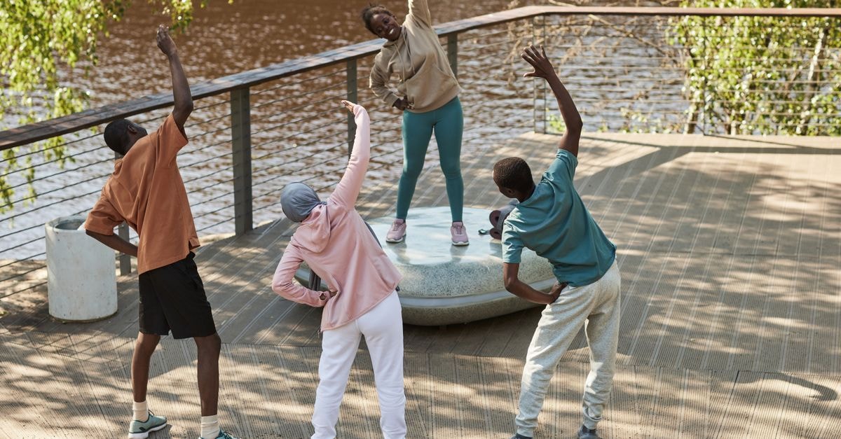 Tieling Travel Guide: Park Mornings and Flexible Layers Four adults stretch and exercise outdoors near a riverside park, enjoying a healthy lifestyle.