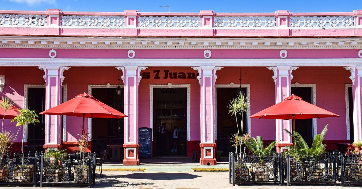Sunlit pink café with red umbrellas in Remedios, Cuba, showcasing colorful colonial architecture.