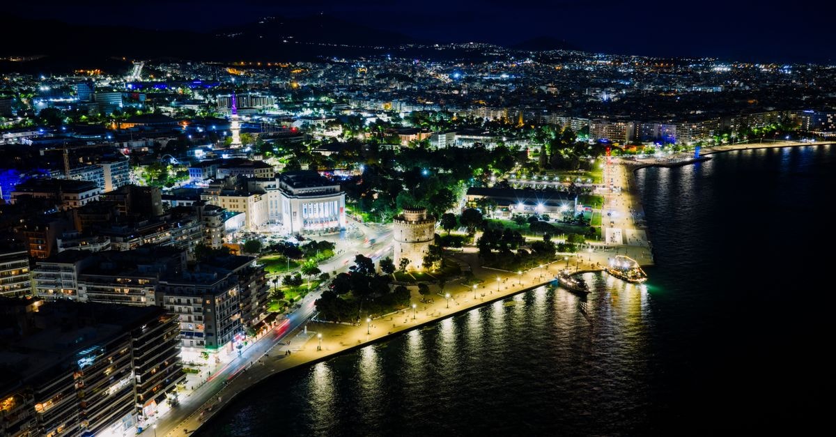 Imperial Plus, Thessaloniki: A Smart Stay on Egnatia Aerial view of Thessaloniki, Greece at night featuring the illuminated White Tower and waterfront.