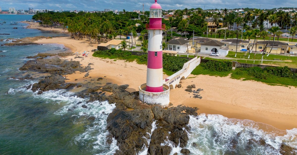 Bata travel guide: weather and arrival tips for Litoral's coastal capital A vibrant aerial shot of the iconic Farol de Itapuã lighthouse along Salvador's coastline with lush greenery.