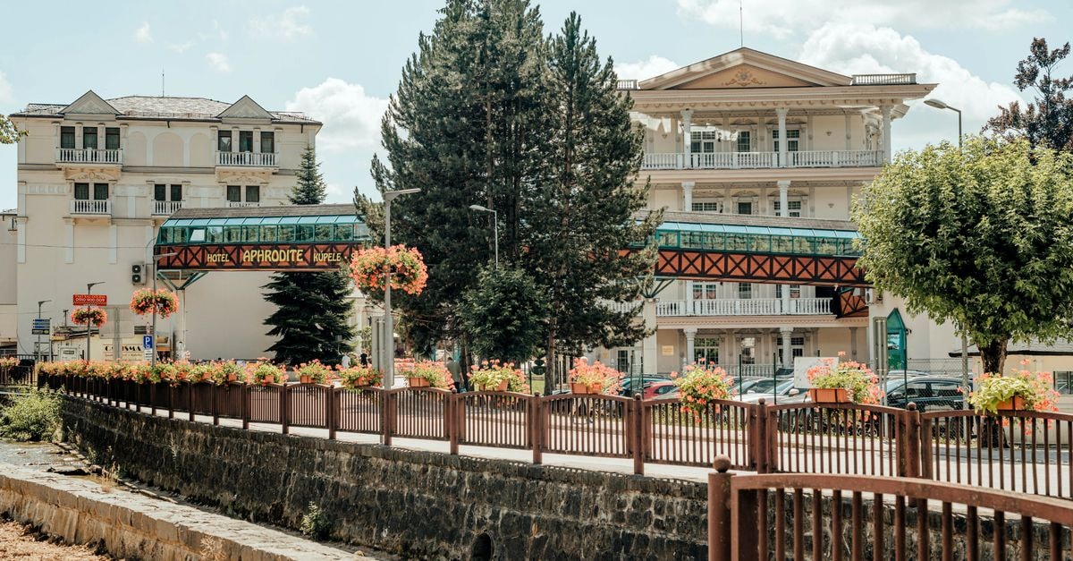 České Budějovice Travel Guide: Planning Tips, Costs and Things to Do Exterior view of Hotel Aphrodite surrounded by lush greenery and floral displays under a bright blue sky.