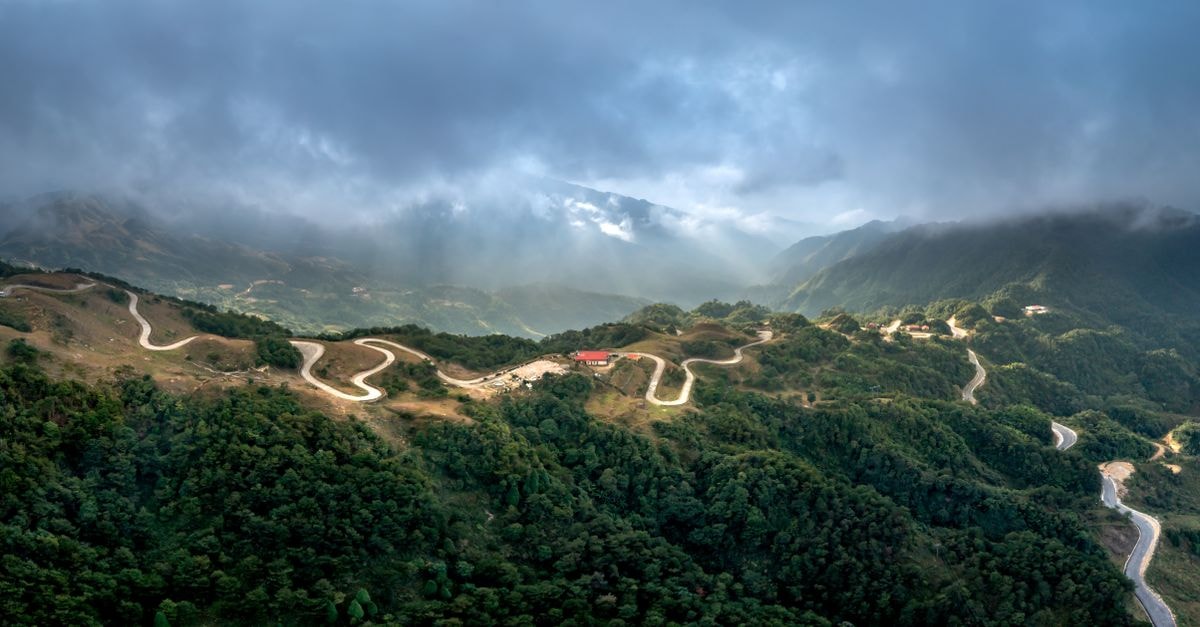Scenic aerial view of a winding road through lush misty mountains.