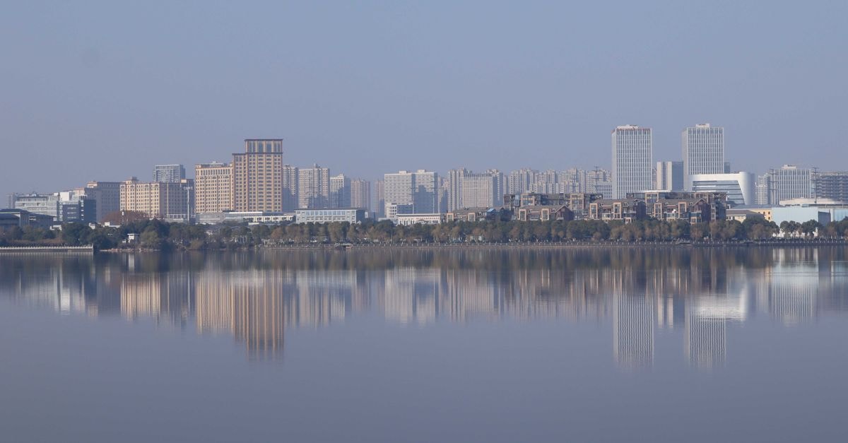 Serene city skyline reflected on calm water under clear sky.
