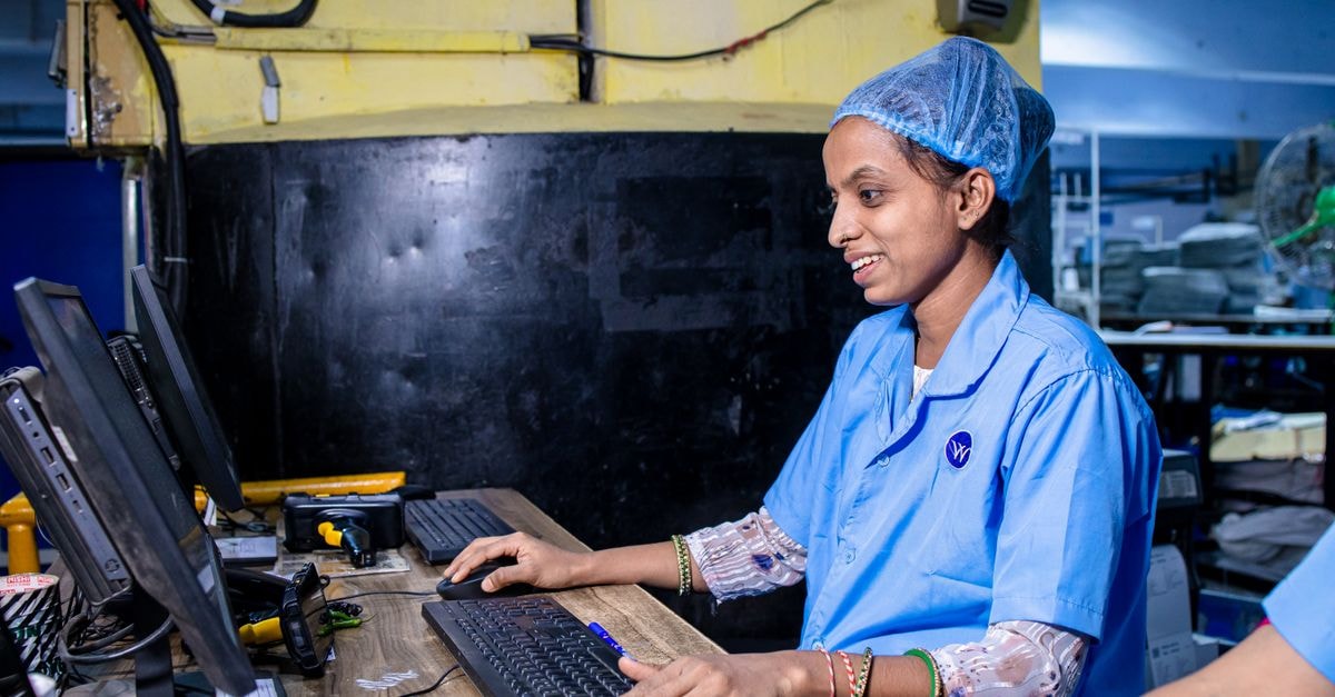 Google tests buying from Walmart-owned Flipkart through Gemini and AI Mode in India Female factory worker in blue uniform operating a computer in a textile factory.