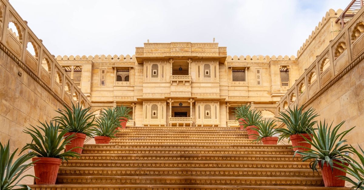 Stunning sandstone palace entrance in Jaisalmer, Rajasthan, India, with ornate steps and potted plants.