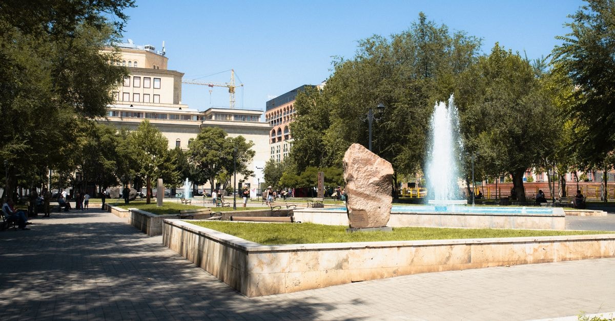 Ramada Hotel & Suites by Wyndham Yerevan: Steps from Charles Aznavour Square A bustling urban park with a central fountain and people enjoying a sunny day.