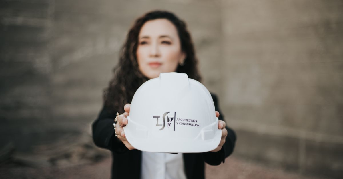 Construction Partners: Strong Quarter, Stretched Price A female architect presenting a hard hat featuring a construction logo, symbolizing professionalism.