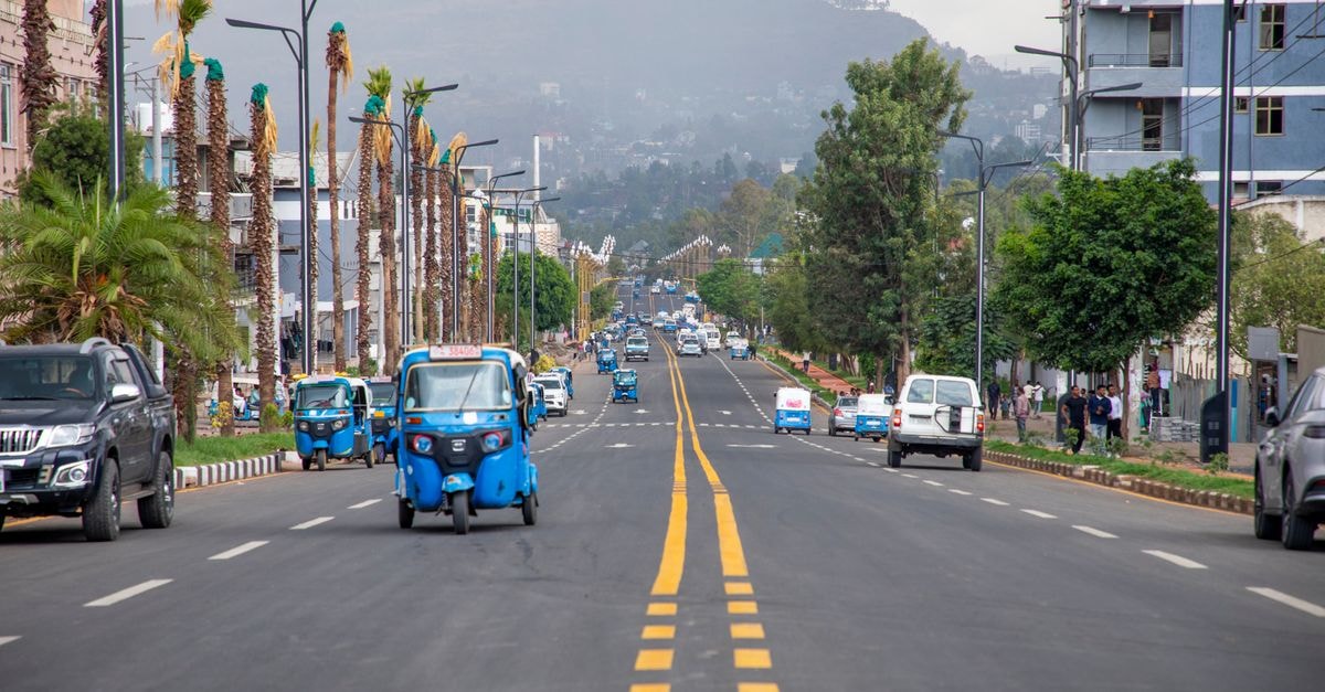 Busy street in Gondar, Ethiopia with blue tuk-tuks, palm trees, and mountain backdrop.