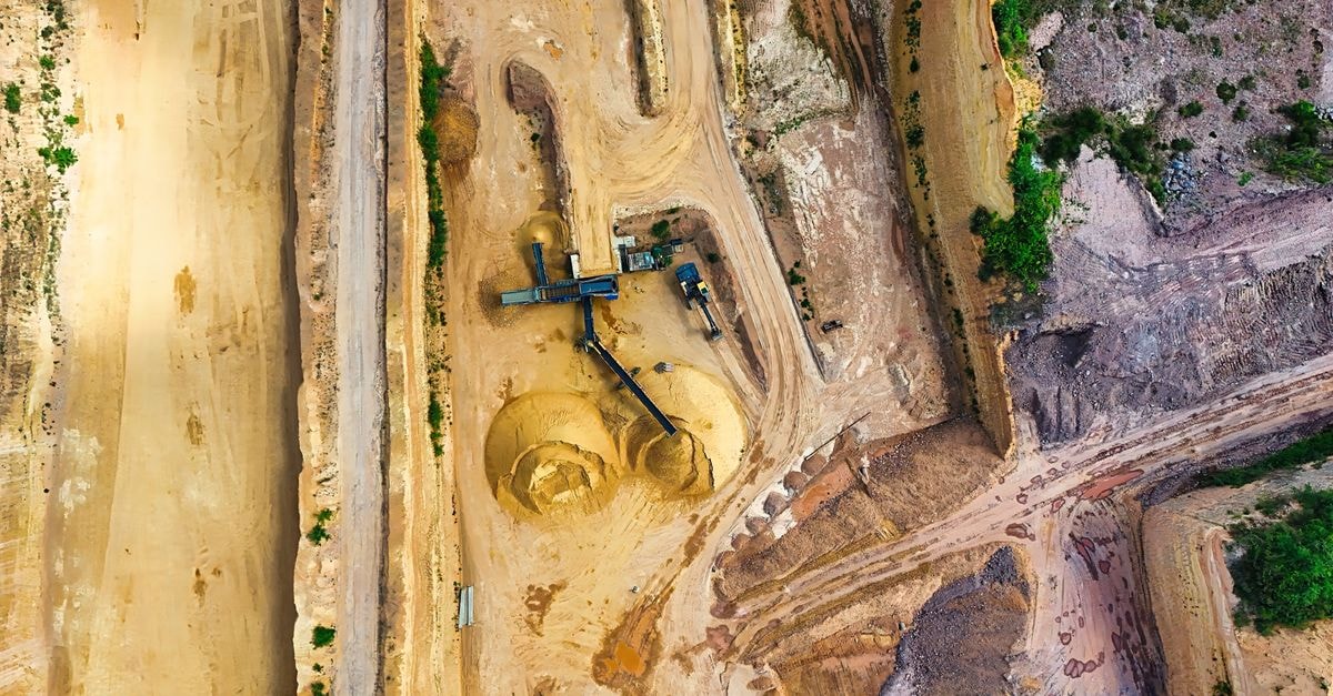 Tungsten Mining Hires Cutfield Freeman to Arrange Debt Funding for Watershed Project An aerial shot of an open-pit mine with machinery and pathways visible, surrounded by landscape.