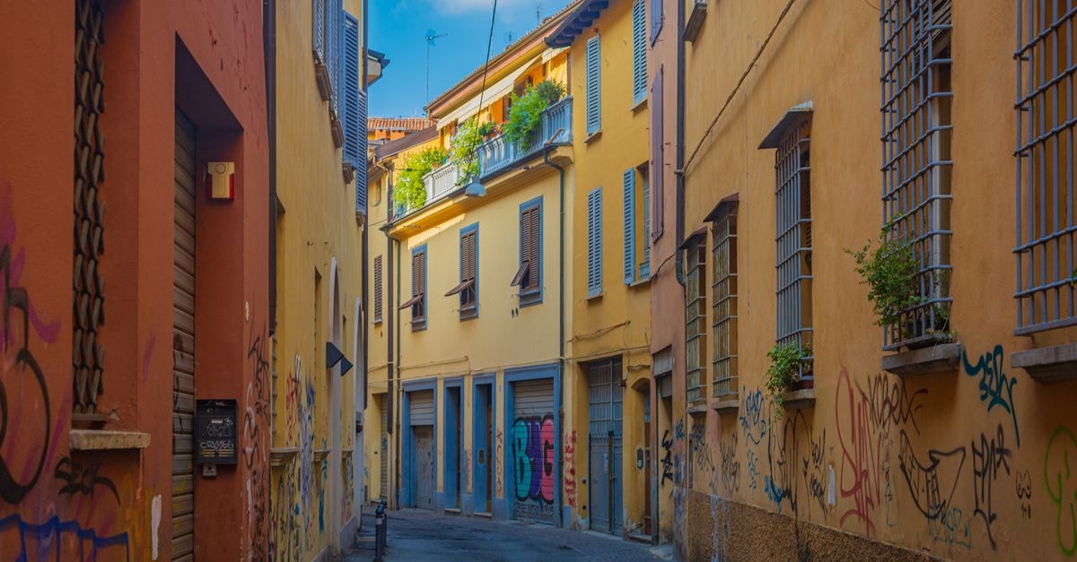 Discover a vibrant alley in Bologna with colorful graffiti and classic Italian architecture.
