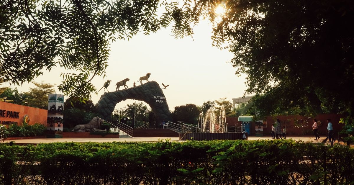 Visitors stroll by the Nature Park entrance under a scenic sunset, surrounded by lush greenery.
