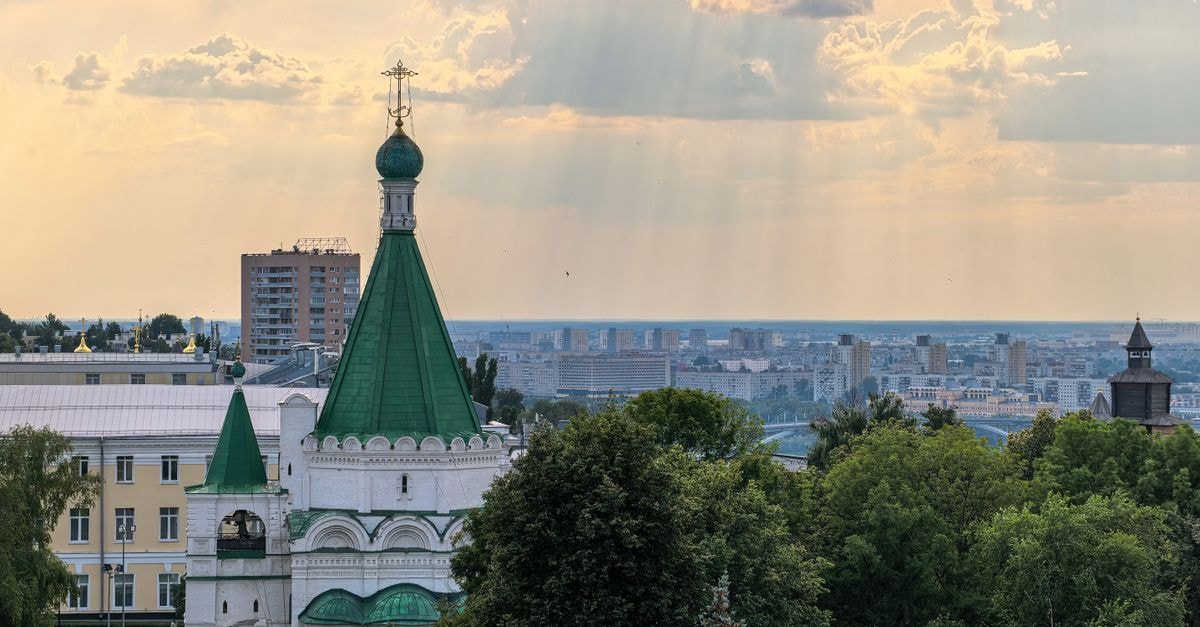 Scenic view of an Orthodox church with green dome and urban skyline during sunset with sun rays.