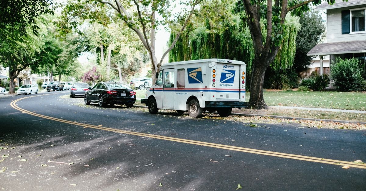 Postal Realty Trust: USPS-Backed Income at a Re-Rated Price A postal delivery van parked on a tree-lined suburban street, showcasing daily mail service.
