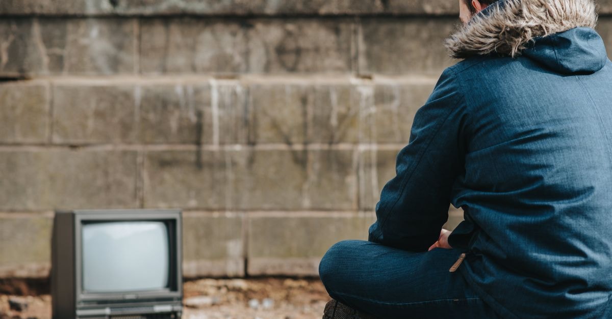 Wonder Man and Booster Gold both cut as Disney+ and HBO Max pull back on superhero TV Back view of anonymous male sitting on ground on street with concrete barrier with graffiti while looking at screen of old fashioned television