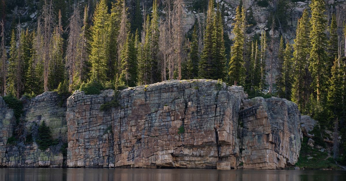 Breathtaking view of a rocky cliff with coniferous trees reflecting off a serene lake in Kamas, Utah.
