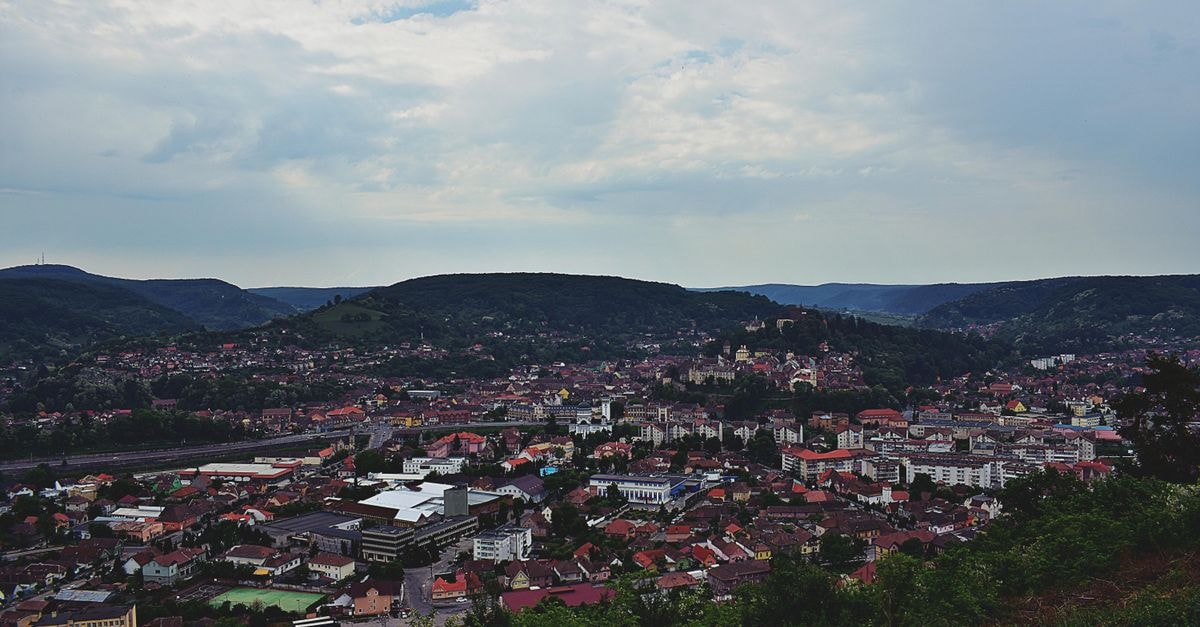 Vila Stanišić in Požega: Quiet Stay Near the Main Square Aerial view of a cityscape surrounded by rolling hills under a cloudy sky.