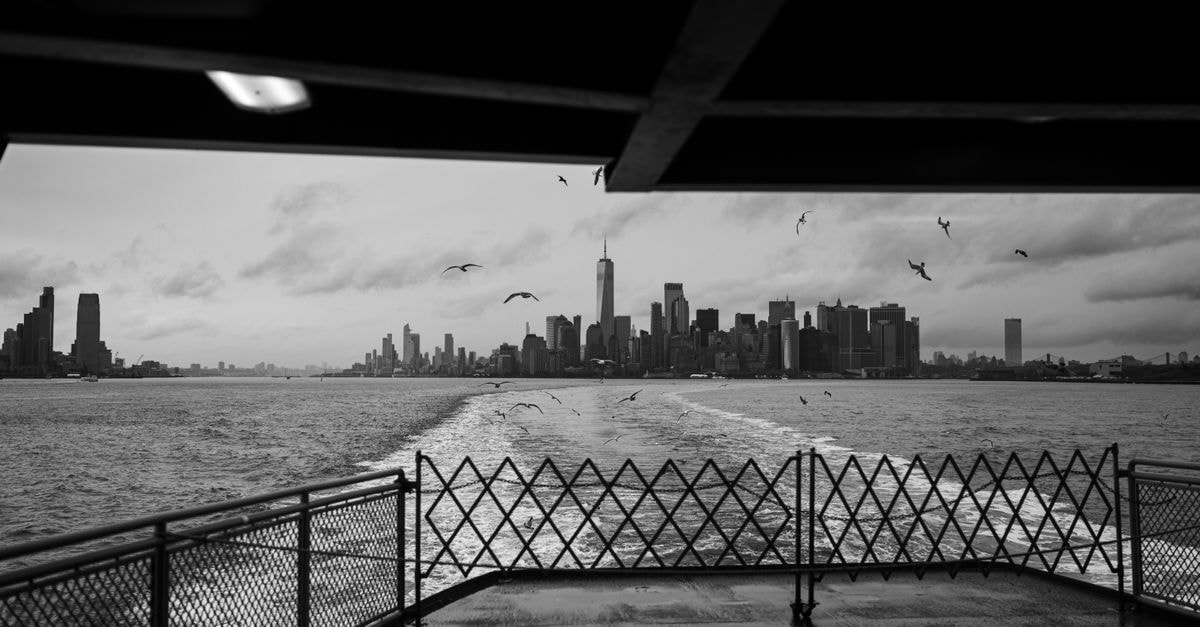 A monochrome skyline of New York City seen from a ferry, highlighting the iconic skyscrapers.