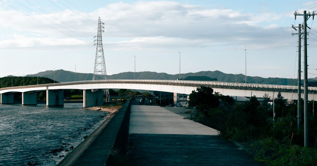 Toyota City Travel Guide: Aichi's Inland Gateway Wide view of a modern bridge spanning a canal in Toyohashi, Japan, with mountains in the background.