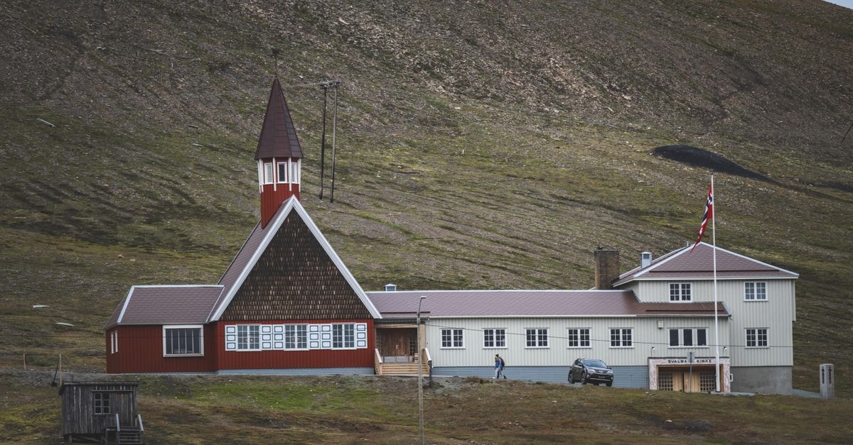 Radisson Blu Polar Hotel, Longyearbyen — The World's Northernmost Full-Service Hotel A scenic view of a red church in Svalbard, Norway, set against a mountainous landscape.