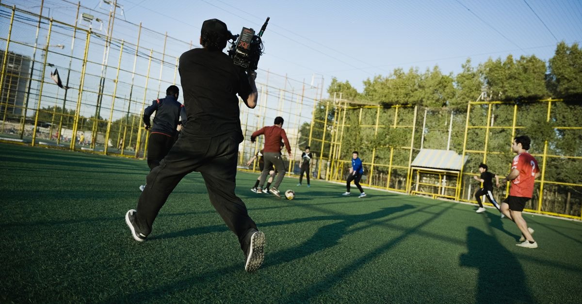 Cameraman captures an outdoor soccer game with players in action on a sunny day.