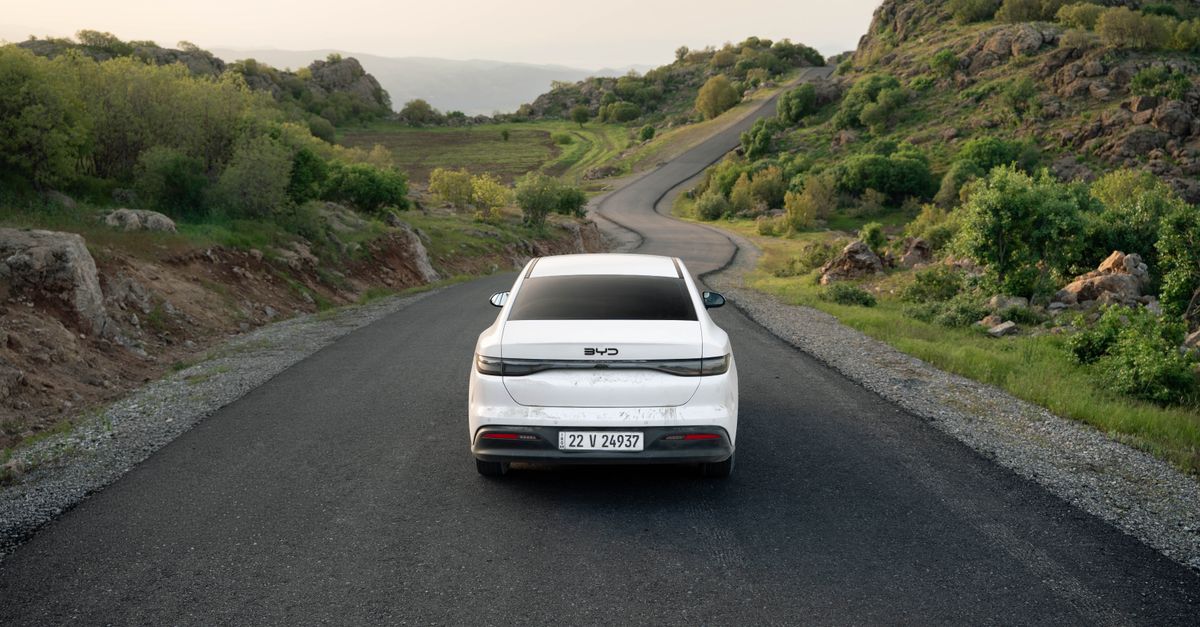BYD, Changan, and Windrose advance on range, sodium chemistry, and electric freight A white car travels down a winding road in the lush hills of Shaqlawa, Iraq, showcasing serene scenery.