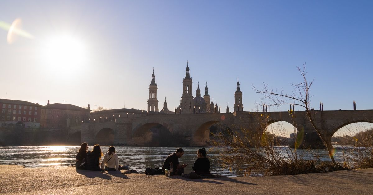 Hotel Reino de Aragón, Zaragoza — A Central Coso Stay with Parking and 24-Hour Gym People relax by the river with Zaragoza's iconic Basilica de Nuestra Señora del Pilar in the background.