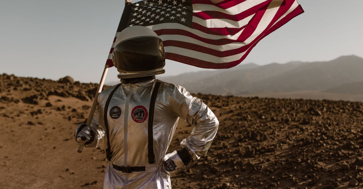 The Odyssey closes in on $200M North American milestone as Nolan posts biggest opening of his career Astronaut in a silver suit holding an American flag, standing on rocky terrain resembling Mars.