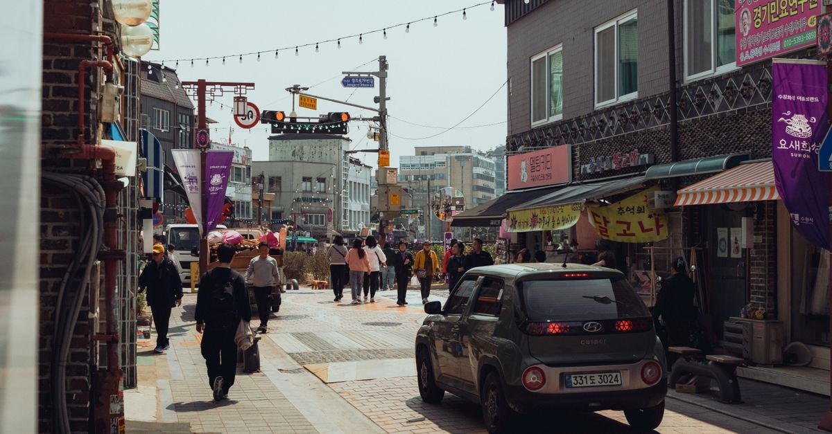 Explore a bustling street scene in Suwon, South Korea, featuring people, shops, and vibrant signage.
