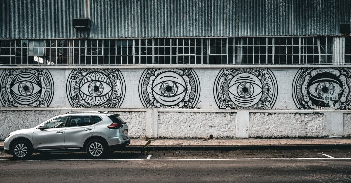 Laventille travel guide: steelpan, murals, and everyday Trinidad Street art mural featuring eye designs on warehouse wall with a silver SUV parked in front.