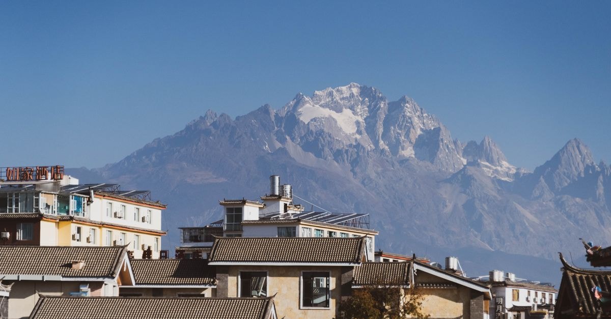 Zhaotong Travel Guide: Yunnan Plateau City Worth a Slow Stop Charming town with traditional roofs against majestic snow-capped mountains on a clear, sunny day.