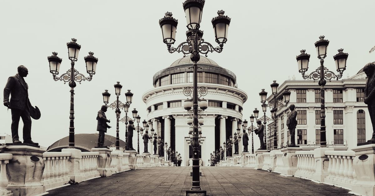 Monochrome view of a bridge with classic lamp posts and statues leading to a grand building in Skopje.
