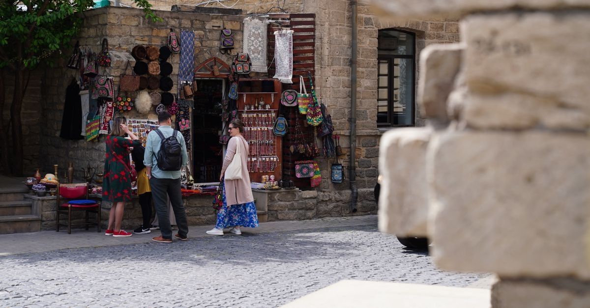 Tourists explore a vibrant street market stall with handcrafted goods in an old stone building setting.