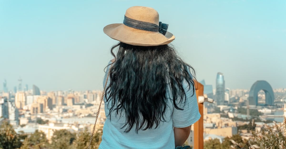 Sumqayit Travel Guide: Caspian Views and City Stays A woman with a straw hat gazes at the stunning skyline of Baku, Azerbaijan on a sunny day.