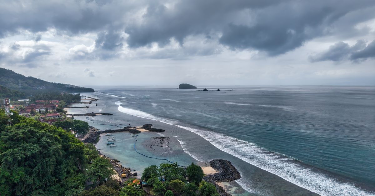 Padang Travel Guide: Planning Tips, Costs and Things to Do Stunning aerial view of Bali's coastline with lush greenery and ocean waves on a cloudy day.