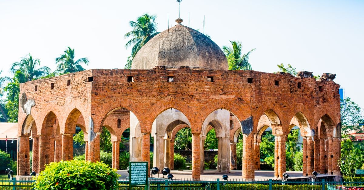 Ancient brick dome with arches in lush outdoor setting in Kalna, India.