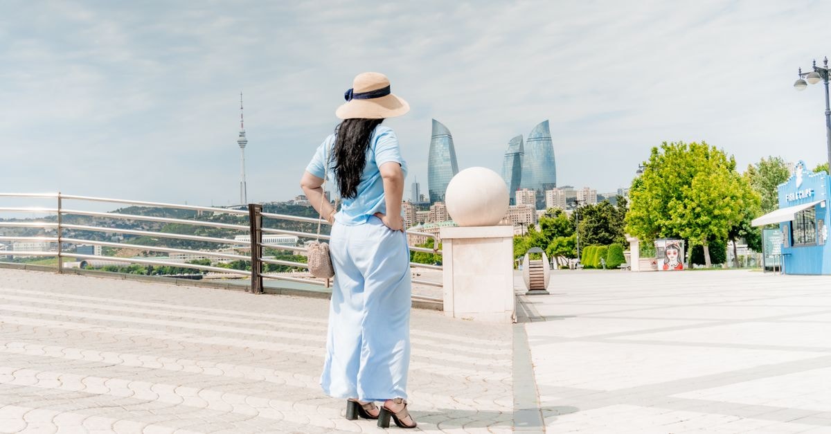 A woman in a sunhat and blue dress stands overlooking Baku's skyline with the iconic Flame Towers.