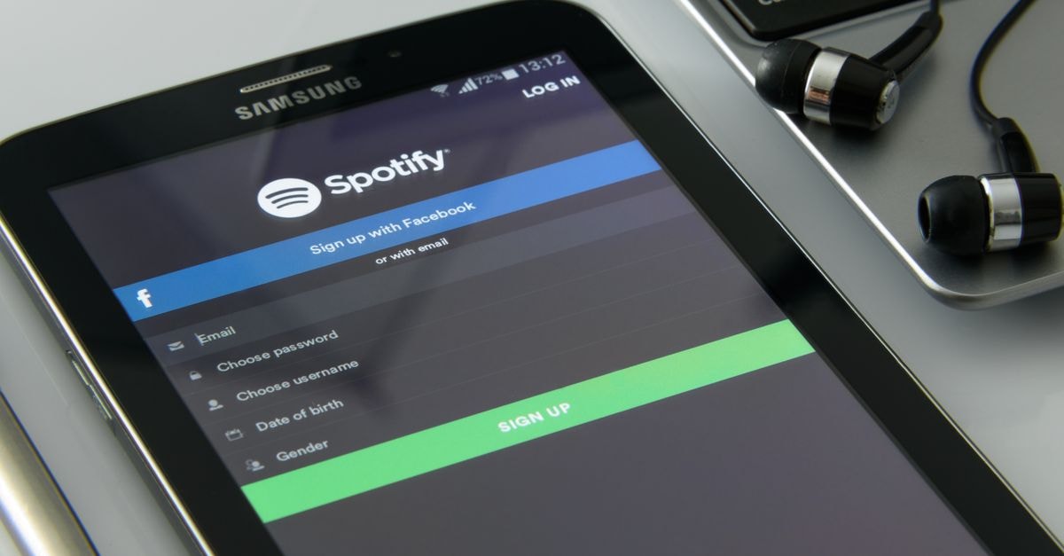 Smartphone showcasing Spotify login screen beside laptop and earphones on desk.