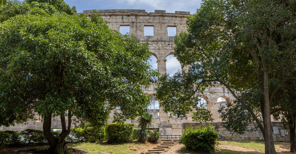 Pula Travel Guide for July 2026: Roman Ruins, Beaches and Istrian Food A serene view of the ancient Roman amphitheater in Pula, Croatia, framed by lush green trees.