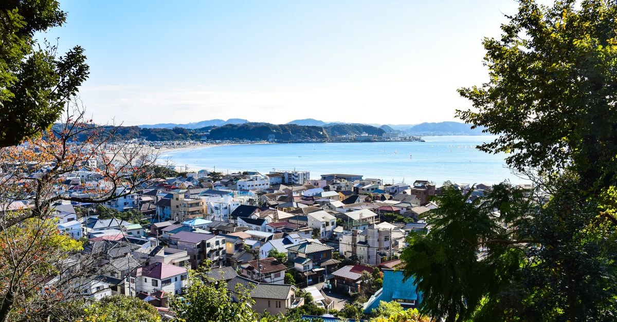 The Gen's Hotel in Hamamatsu: Steps from the Station and a Bathhouse Vibe View of a picturesque coastal town framed by lush greenery and calm sea, showcasing natural beauty.